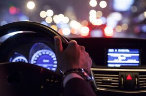 View of steering wheel and car dashboard as a driver operates a vehicle at night while heeding New Year’s Eve road safety tips.