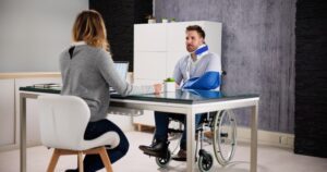 An injured man in a wheelchair, wearing a neck brace and an arm sling, meeting with an experienced car accident lawyer in Fresno.