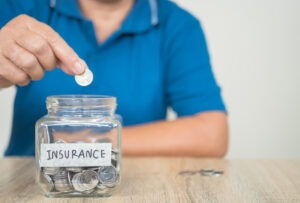 A person places a coin in a jar labeled “insurance,” which could be an example of someone not using insurance money for repairs.