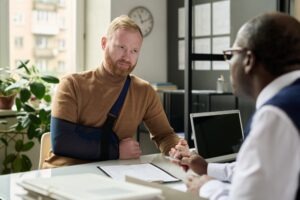 Man with his arm in a sling speaking with a lawyer about the legal fees for a car accident lawsuit.