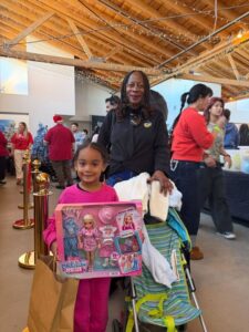 Mother and young daughter smiling as the girl holds up the new doll set she received at the Holiday Toy Drive with 24LA sponsored by Omega Law Group.